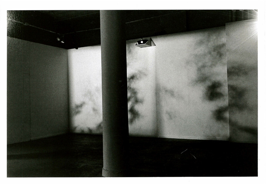 An indistinguishable projection on the wall with an installed light appearing above it facing the opposite direction and a bright light coming in from the upper right corner of the image. A column bisects the image.