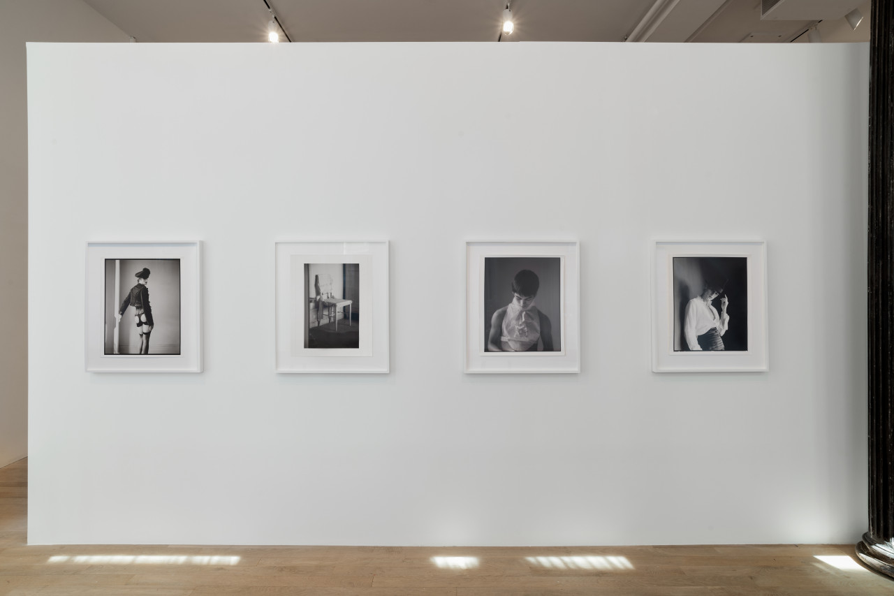 Four black and white photographs hang on a gallery wall. The floor is speckled with light, and the photographs, mainly portraits, are dramatic yet soft.