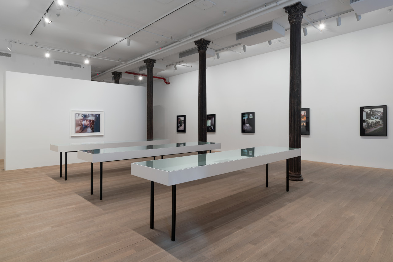 In an open gallery space, three vitirnes stand surrounded by walls displaying large color photographs with thick black borders.