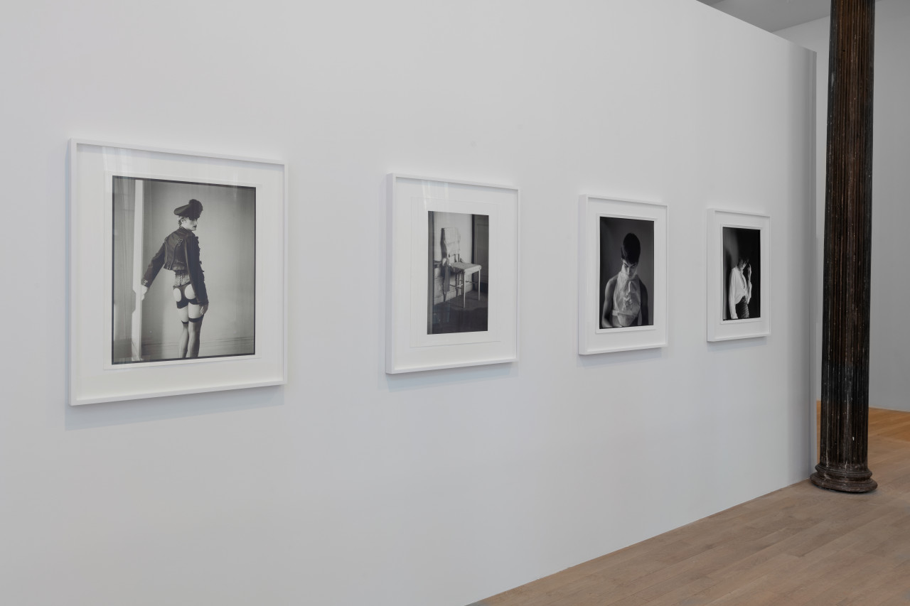 Four black and white photographs hang vertically on the gallery wall. The images, three of which are portraits, the other of a chair, share a similar tone of drama and quietness as only one subject is given focus at a time.