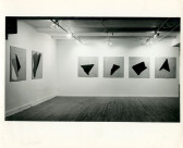 A black and white installation photograph of six paintings with dark geometric forms in a gallery space.