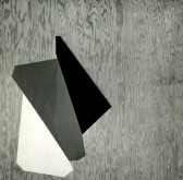 A black and white photograph of three forms over a wooden background. The forms are vaguely triangular and are white, grey, and black.