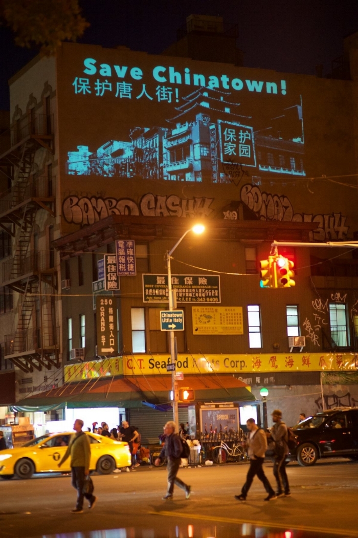 A view of Chinatown at night, with a projection onto the side of a building which reads 