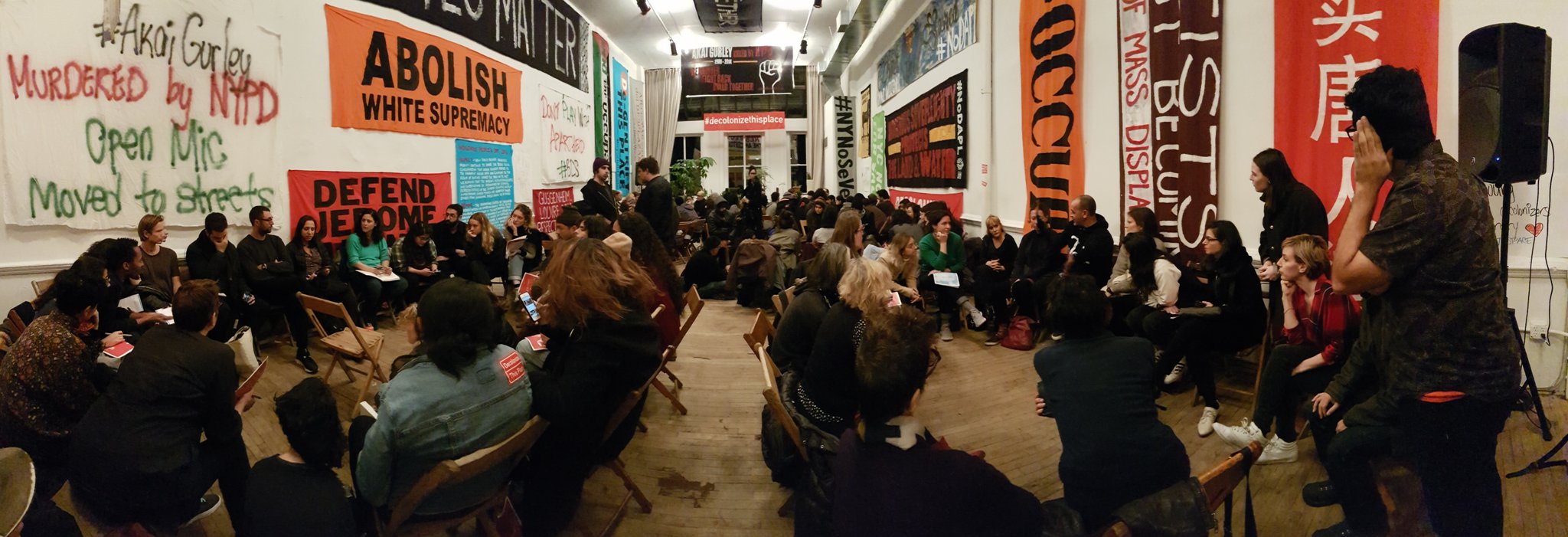 View of the audience at the Artists Space and Decolonize This Place event, with banners of resistance posted along the walls. One visible reads 