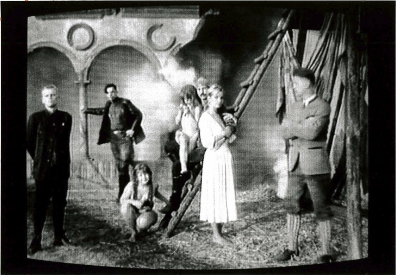 Seven people are in a courtyard in period dress, facing the camera.  Some stand on a ladder, another leans against a colonnade in the background.  Smoke billows out behind them from an unseen source.
