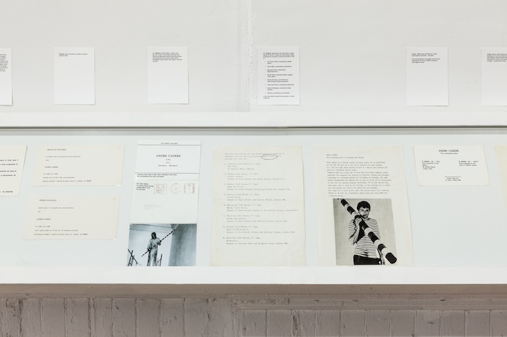 A book shelf displays various documents and photographs behind glass. Documents with text hang directly above.