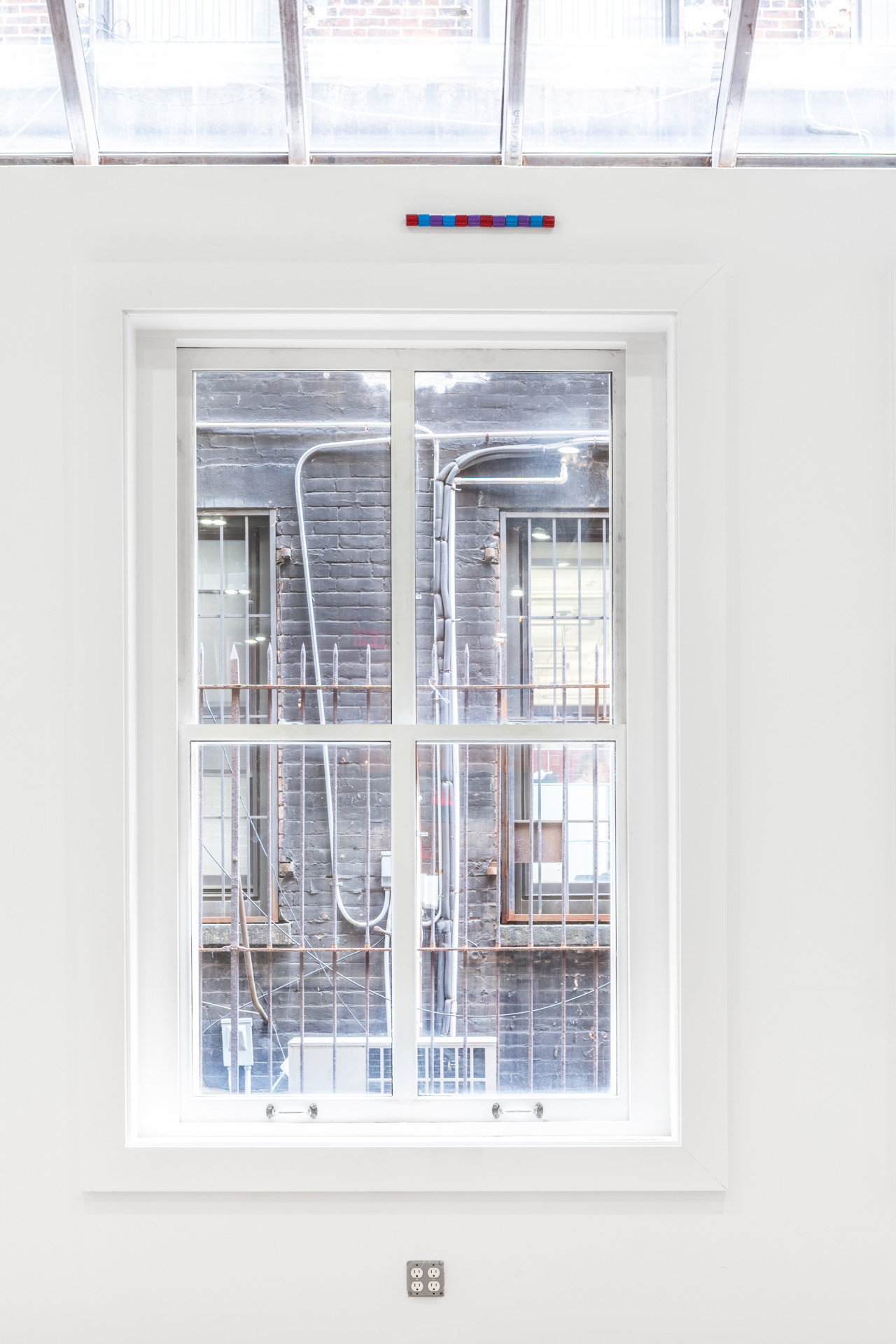 A small strip of pixeled colors is displayed left of center above a large window looking out onto a building.