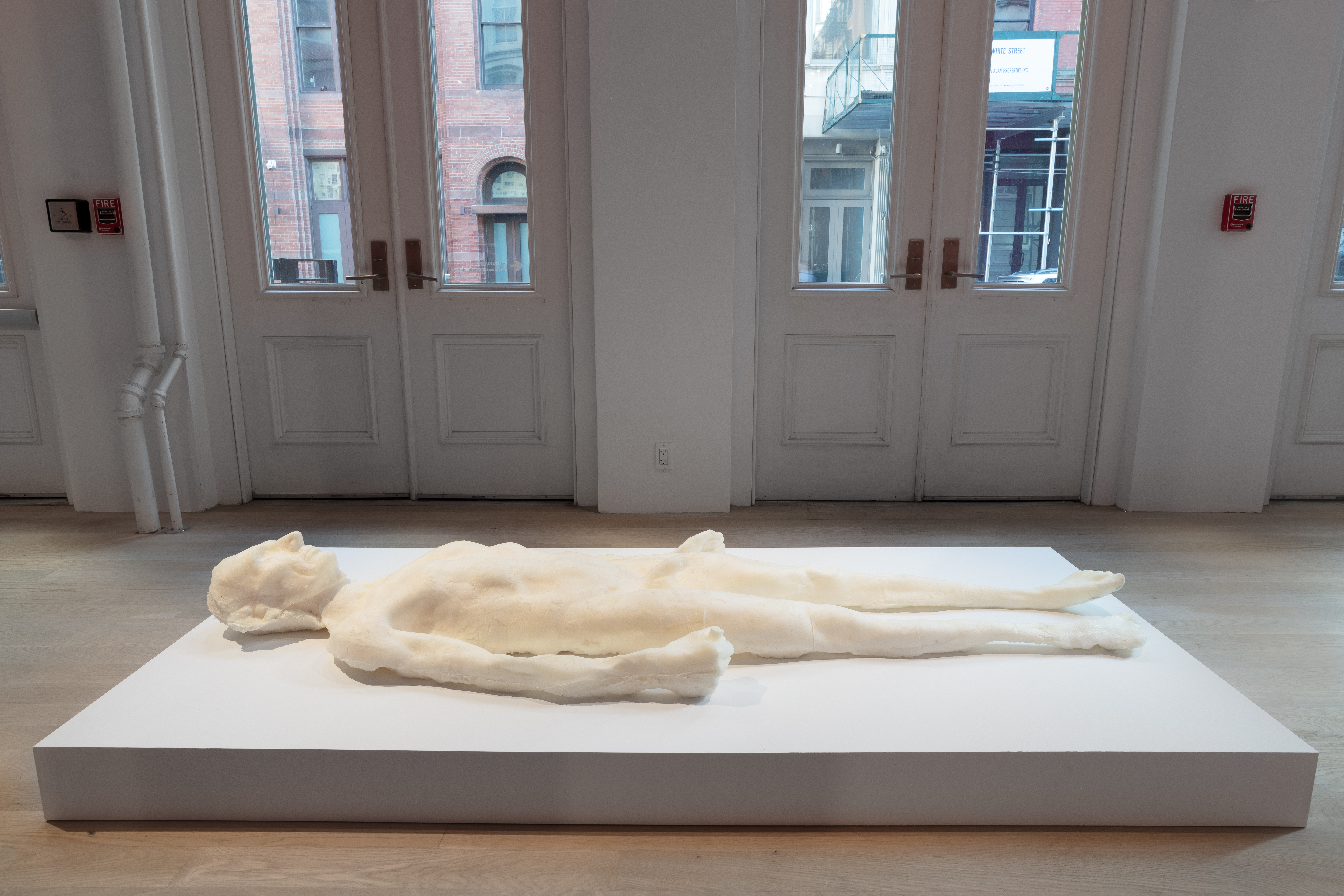 A life-size foam sculpture of a naked human form in the likeness of Abraham Lincoln rests supine on a low white platform.