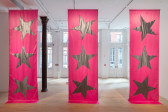 Three large pink fabric banners by Isabelle Frances McGuire, each bearing three silver star patches, hang from the ceiling to rest on the floor.