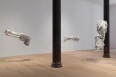Color image of a gallery space with three large white biomorphic sculptures by Ruben Ulises Rodriguez Montoya hanging from the ceiling throughout. The sculptures are composed of discarded car parts, pigmented silicone, animal horns, clothes, and various other found materials.