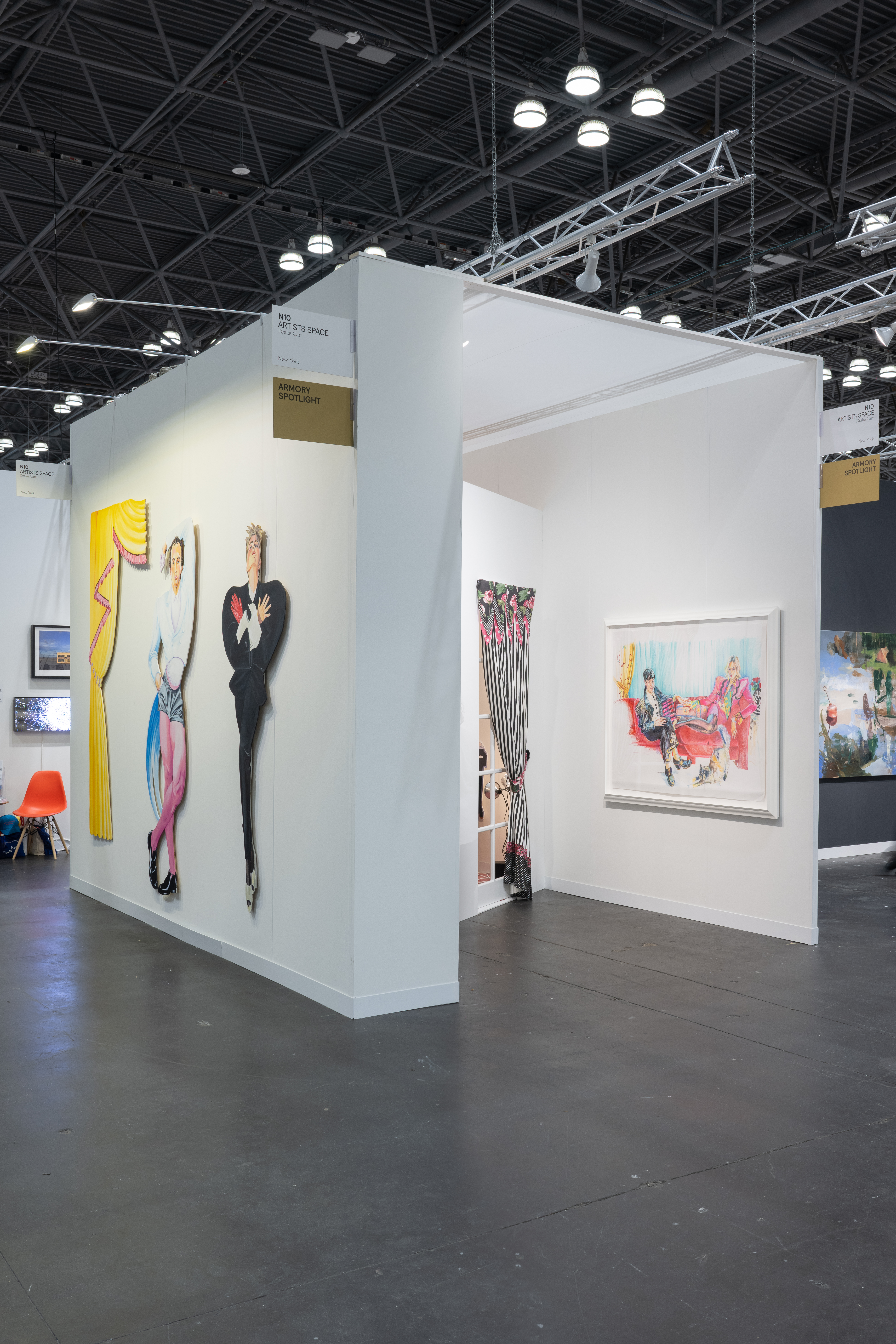 Color image of a side view of a booth inside an art fair. On the outside of the left wall, three works made of cut-out panels can be seen. One is in the shape of curtains, and two are human figures. Inside the booth, a window with balck and white curtains with pink flowers can be seen. On the right wall hangs a colorful drawing with two figures sitting on a couch.