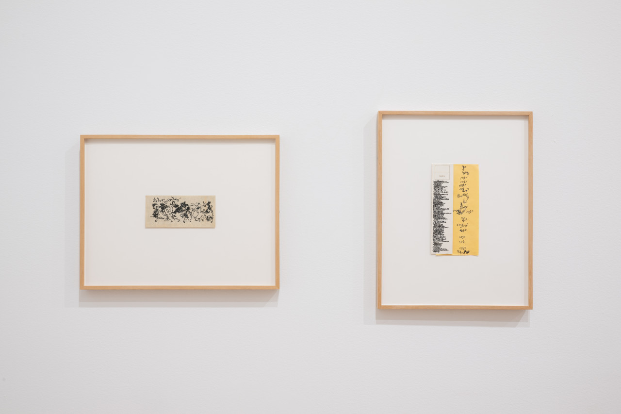 Two works on paper hanging on a white gallery wall. The work on the left features curling black lines that accrete densely in various clusters. The work on the right features two overlapping pieces of paper with a box in the top-left corner that reads "Index." The paper on top is white and features various lines of dense, swirling black calligraphic lines of ink that approximate text, followed by a small printed line of text that reads "(over)." The larger paper beneath is yellowish and features larger, curling lines of black ink.