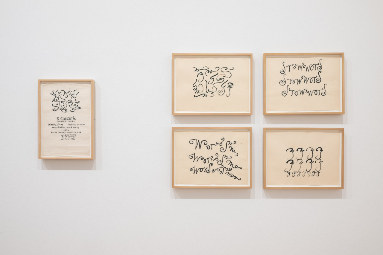 Five framed works on paper, one individual work on the left and a cluster of four on the right, hang on a white gallery wall. Works feature abstract, calligraphic strokes in black ink on paper. Individual work on the left includes hand-painted text reading "3 concerts, improvised music. La Monte Young - sopranino saxophone, Angus MacLise - hand drums, drone, 8-12pm Sundays - August 12, 19, 26, 10-4 Group Gallery, 73 4th Avenue, contribution $1.50"