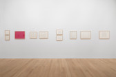 White gallery wall featuring various small framed works on paper, one on pink ground.