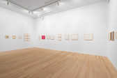 Fish-eye view featuring various clusters of framed works on paper hanging on three white gallery walls.