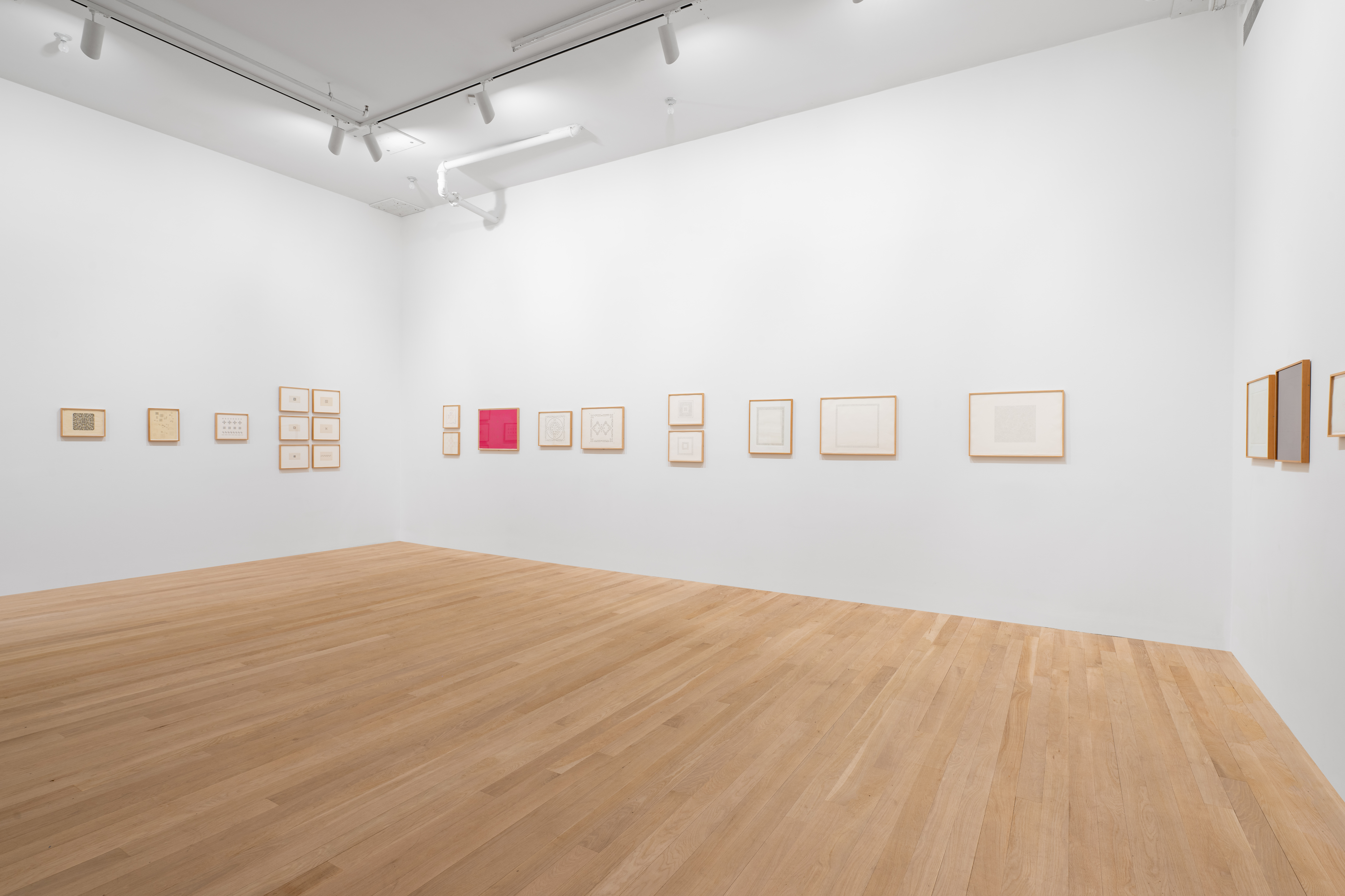 Fish-eye view featuring various clusters of framed works on paper hanging on three white gallery walls.