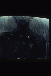 Dark image of the upper torso of a woman with liquid dripping in the foreground of the image.
