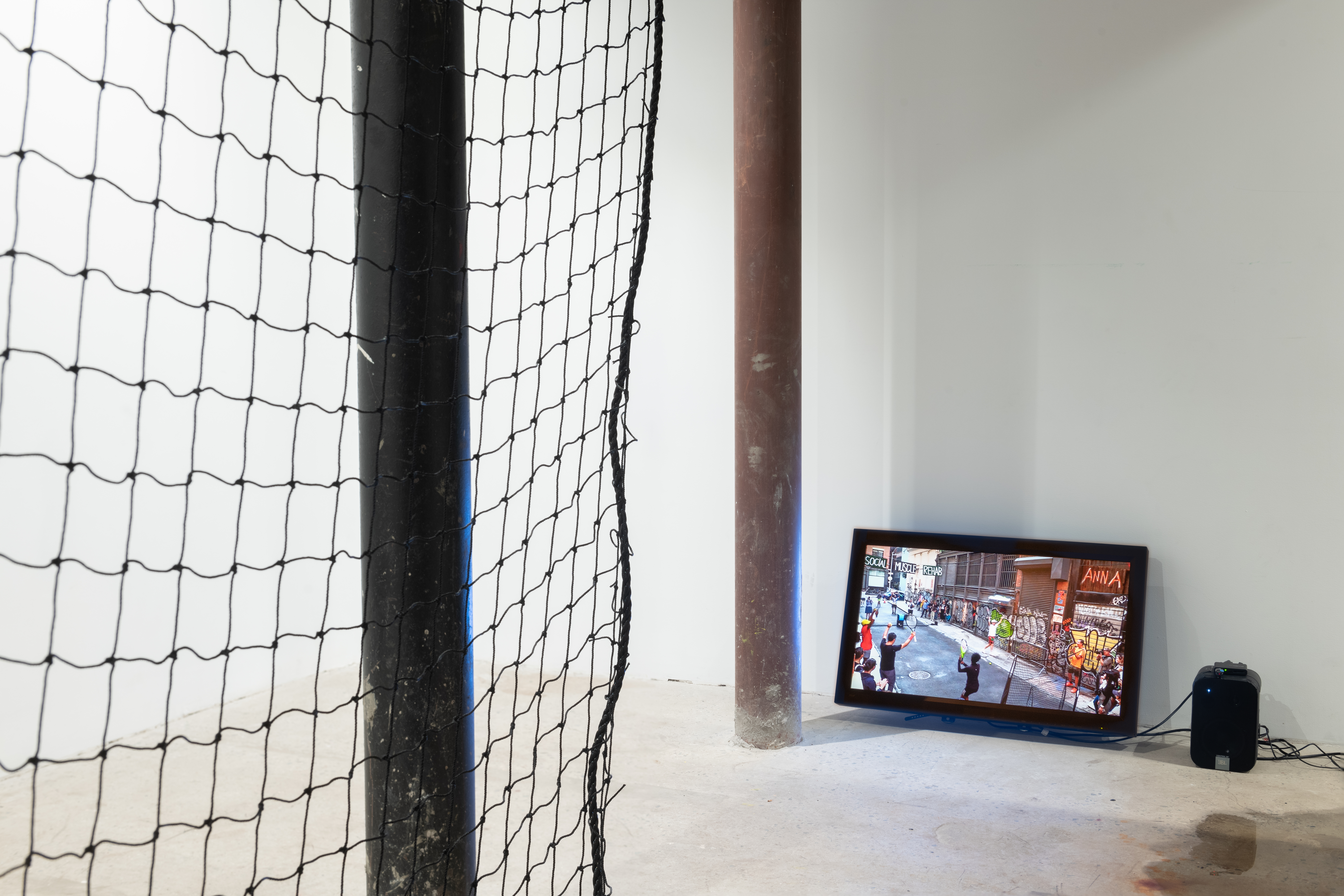 View of a florbound television screen and speaker next to a brown pole. The edge of a black net is visible on the left.