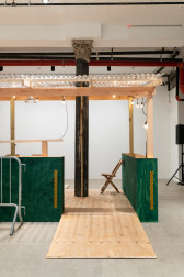 An installation view of a green and tan wooden dining corral with a ramp. A chair and column are visible in the background.