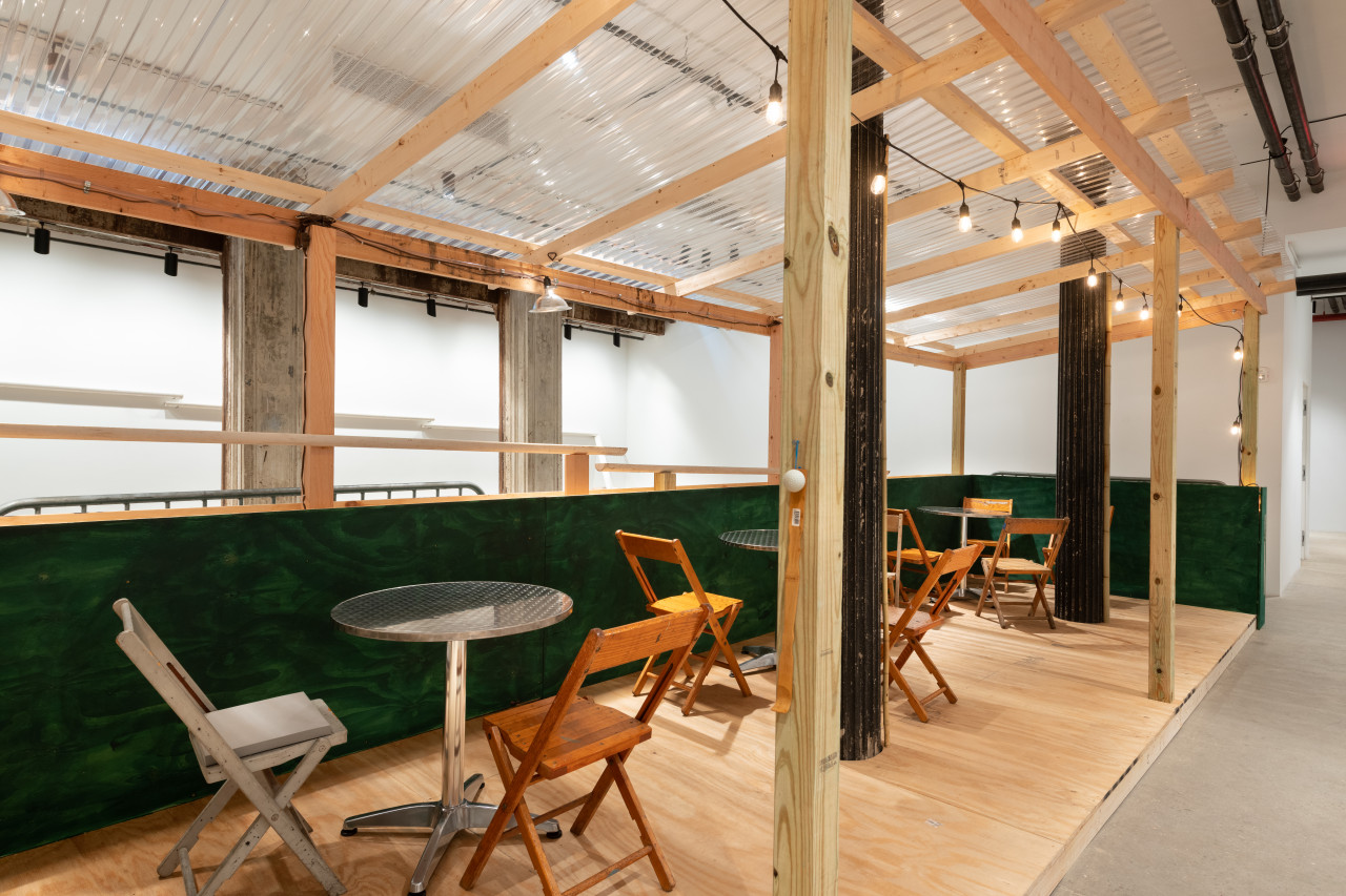 An installation view of a green and tan wooden dining corral with metal tables and wooden chairs.