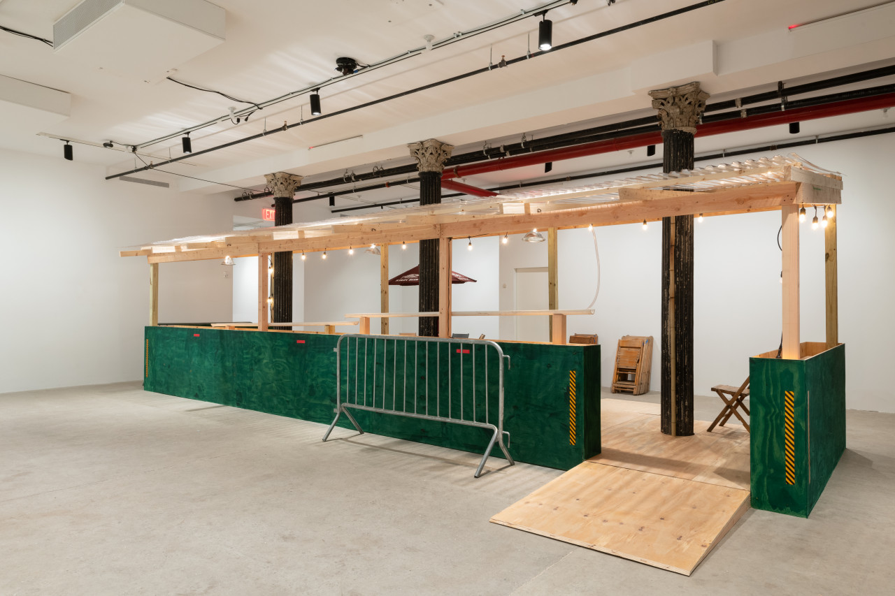 An installation view of a green and tan wooden dining corral with a ramp and a metal barricade.