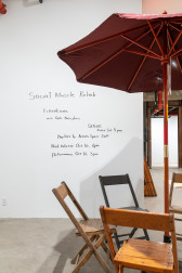 Four wooden chairs around a red dining umbrella. Handwritten in black sharpie, the words 