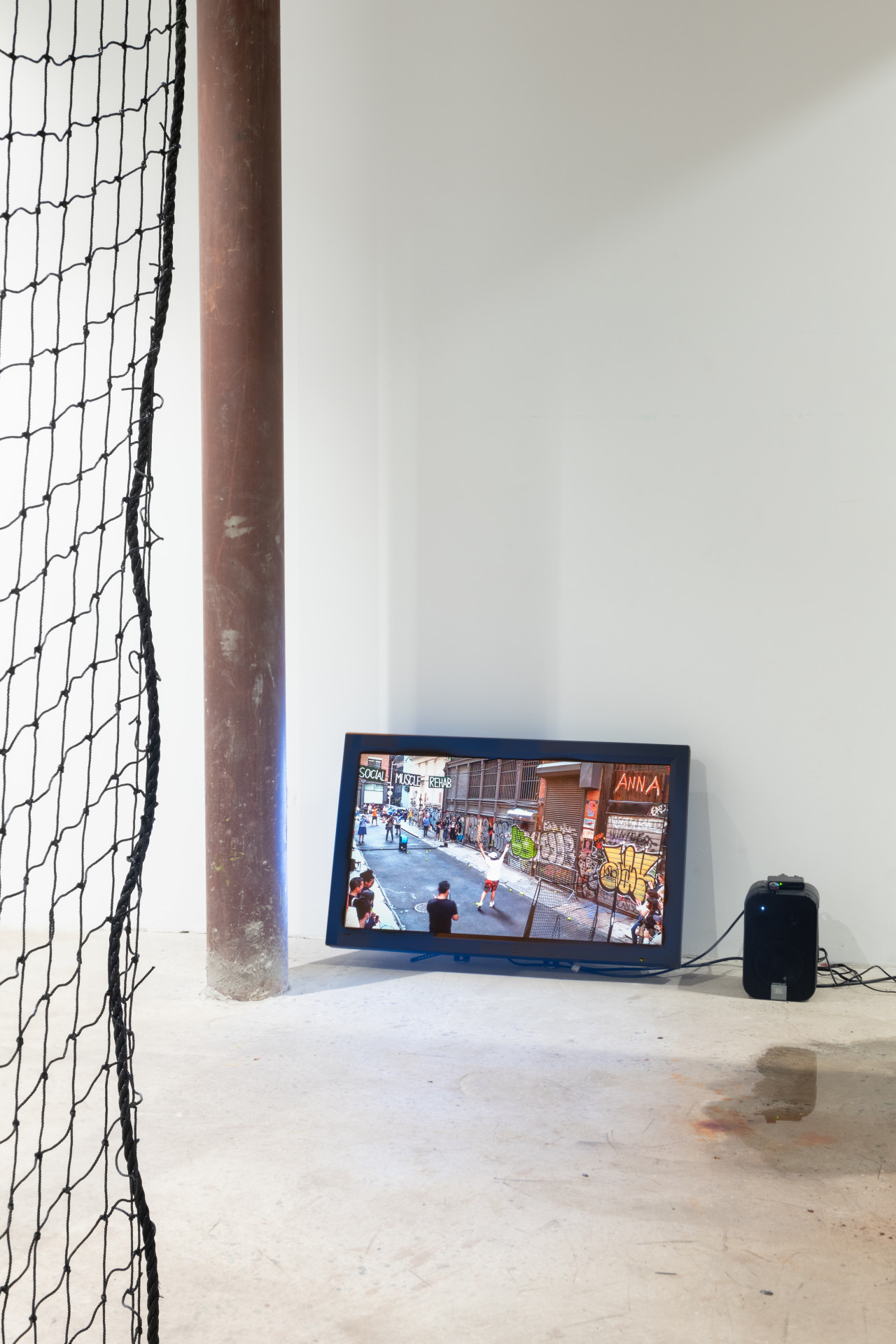 View of a florbound television screen and speaker next to a brown pole. The edge of a black net is visible on the left.
