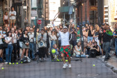A person with a tennis racket wearing a white hat, shirt, and red and green shorts throws his hands up in gleeful celebration. In the background, a crowd behind a net watches intently.
