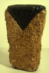 A vertical rectangle of straw on a white background.  The top of the rectangle is covered by an inverted triangle made of black tar.