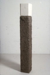 A rectangular column of rough, brown material is capped by a smooth cube of white stone.