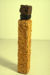 A rectangular column against a white background.  The bottom segment is covered in corn kernals, then there is a layer of black tar, and the top is a cube of copper.