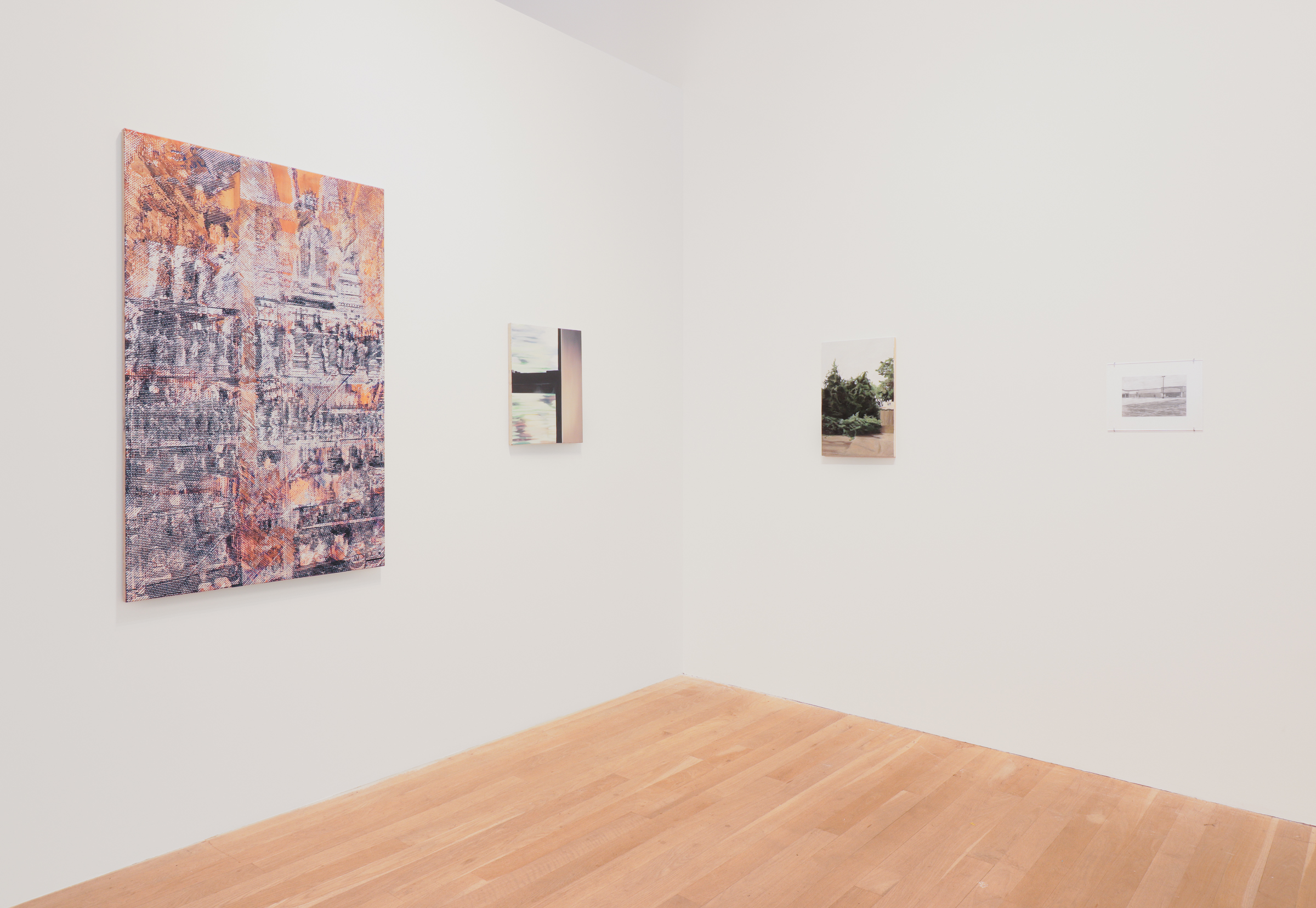Color photograph of a gallery installation view. Two walls converge in a corner: on the left wall is a larger, colorful painting with a smaller one to its right. On the right wall, there is one smaller painting and one black and white image under plexiglass.