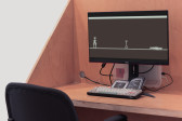 An image showing a video game work consisting of a monitor, a keyboard, and instructional booklet arranged on a wooden desk.