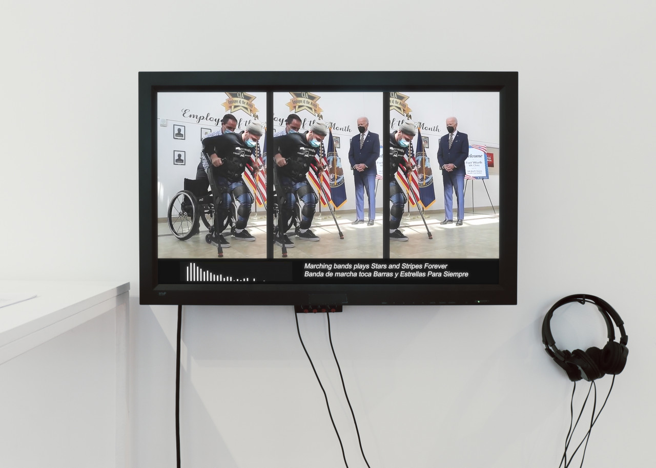 A color photograph of a video monitor mounted on a wall with two headsets hanging nearby