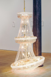 Color installation image showing a chandelier hanging from the ceiling and resting on the floor in front of a dark column.