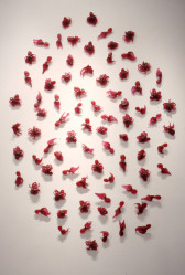 Small red sculptures of octopi and squids arranged in an oval shape on a white wall.
