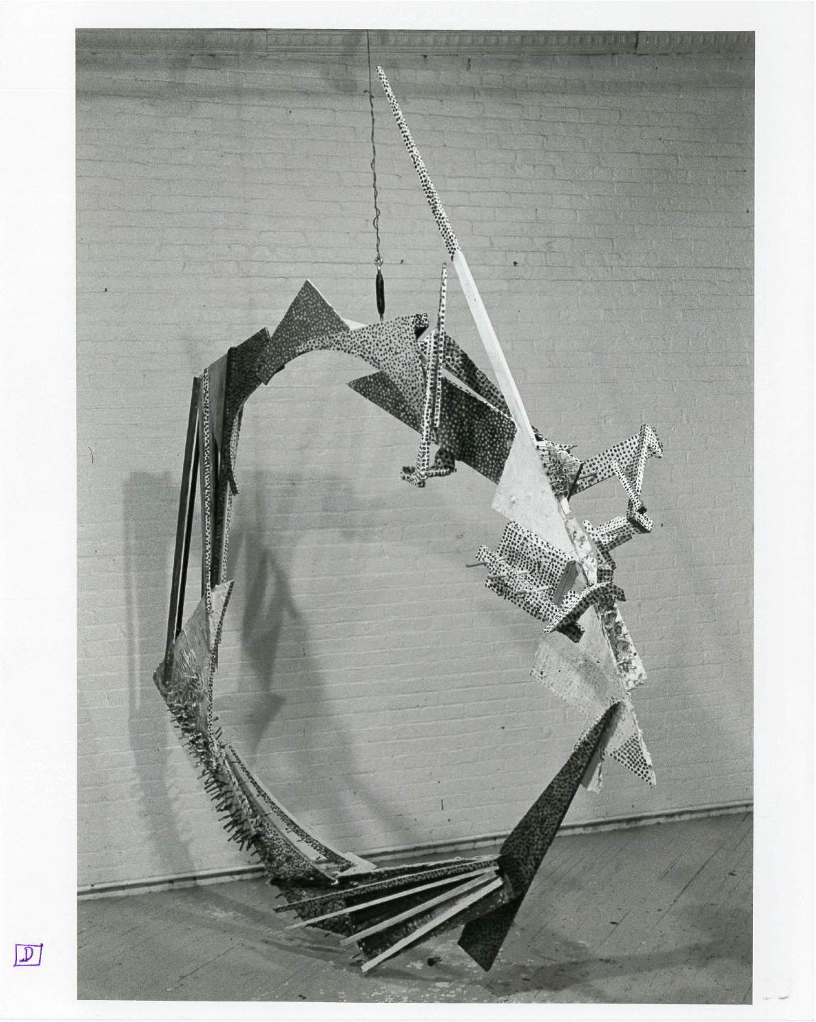 Circular bricolage sculpture in a white-walled gallery space.