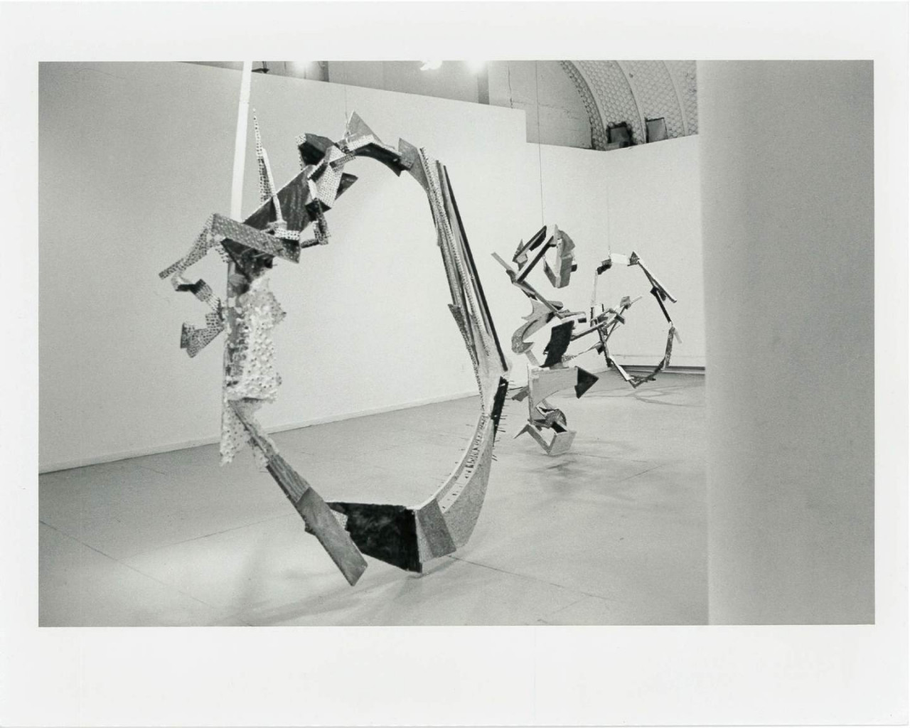 Circular sculptural forms hang from the ceiling and touch the floor in a white-walled gallery space.