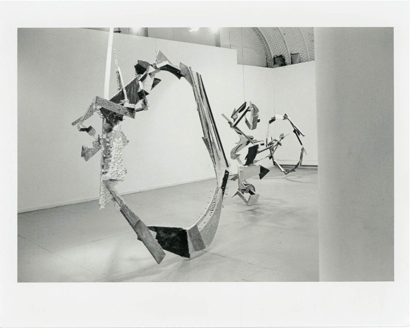 Circular sculptural forms hang from the ceiling and touch the floor in a white-walled gallery space.