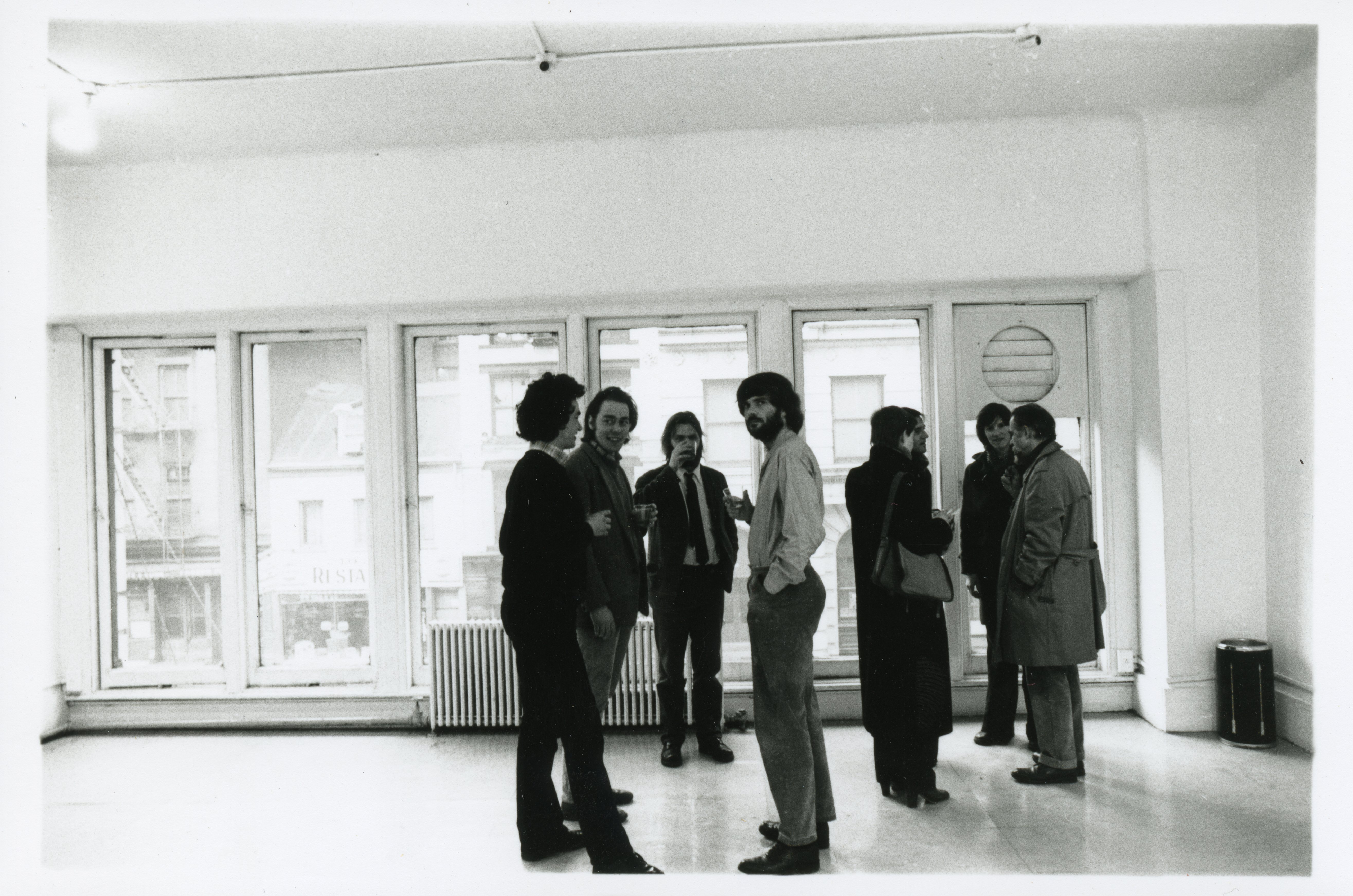 A photograph of the exhibition opening reception. A group of visitors look around at the art.