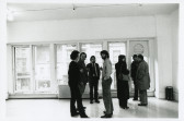 A photograph of the exhibition opening reception. A group of visitors look around at the art.