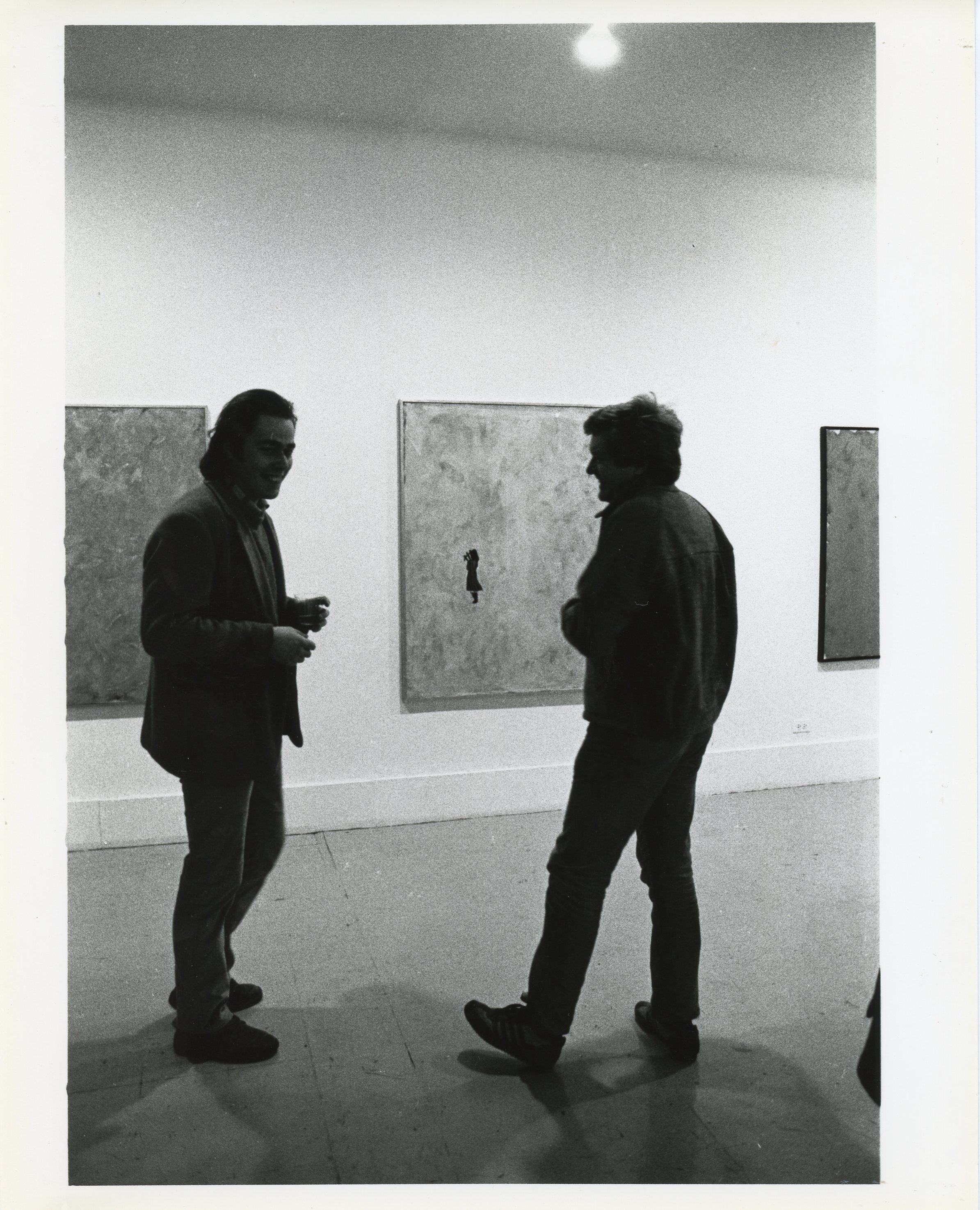 A photograph of the exhibition opening reception. A group of visitors look around at the art.