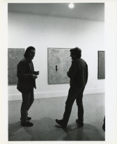 A photograph of the exhibition opening reception. A group of visitors look around at the art.