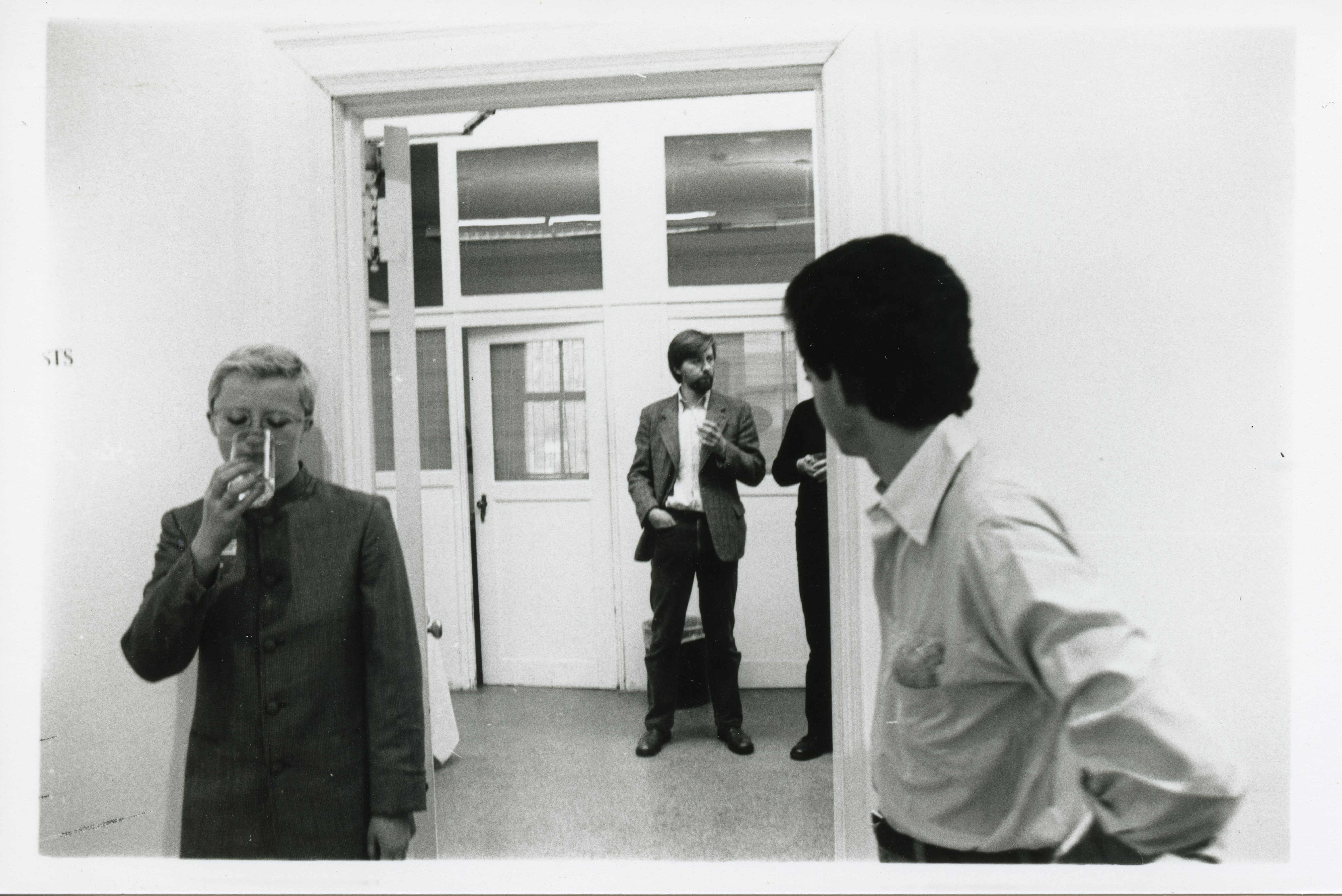 A photograph of the exhibition opening reception. A group of visitors look around at the art.
