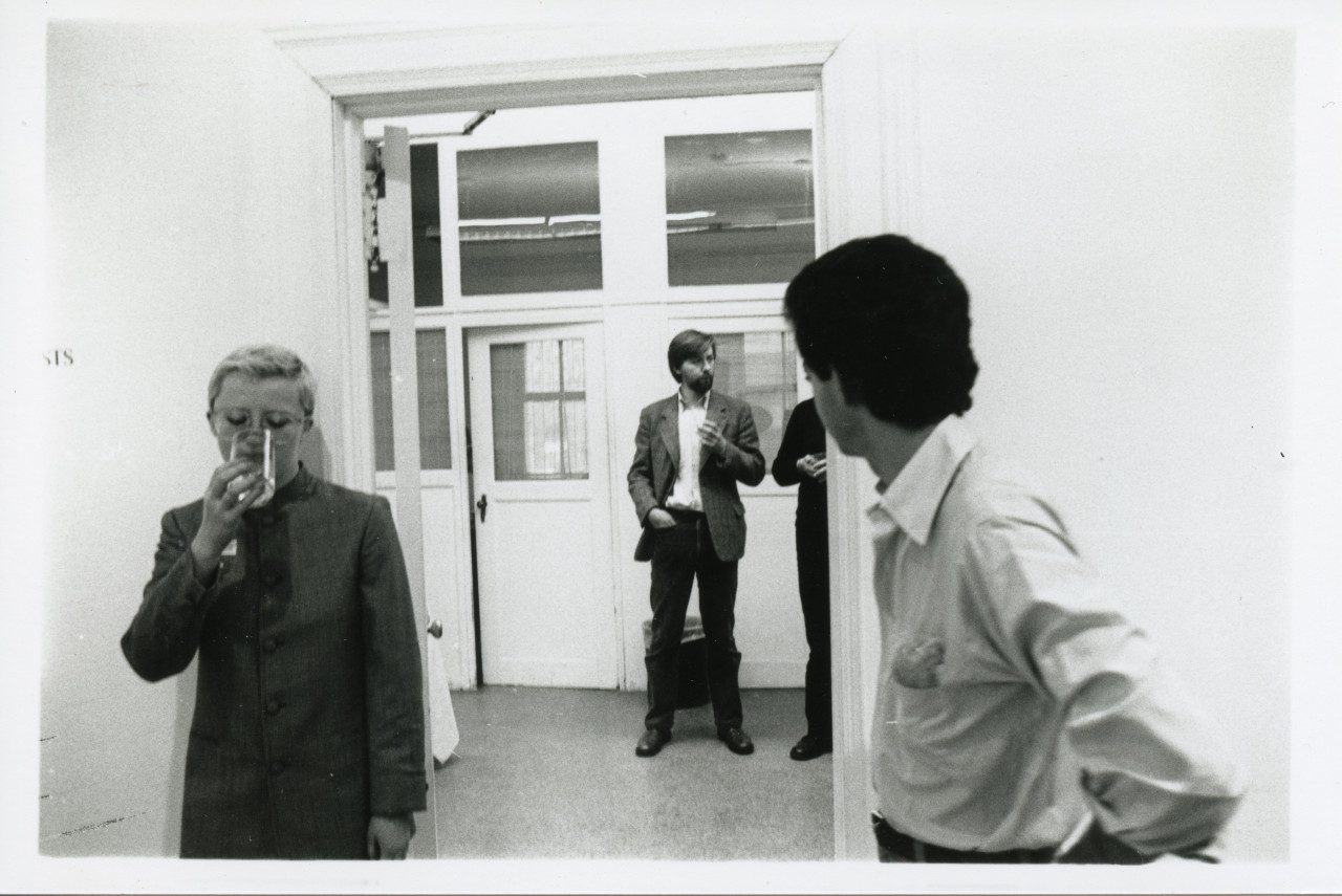 A photograph of the exhibition opening reception. A group of visitors look around at the art.