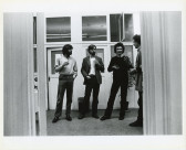 A photograph of the exhibition opening reception. A group of visitors look around at the art.