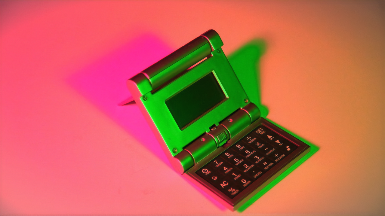 An open folding calculator, turned on its side and illuminated by bright green, peach, and pink lights.