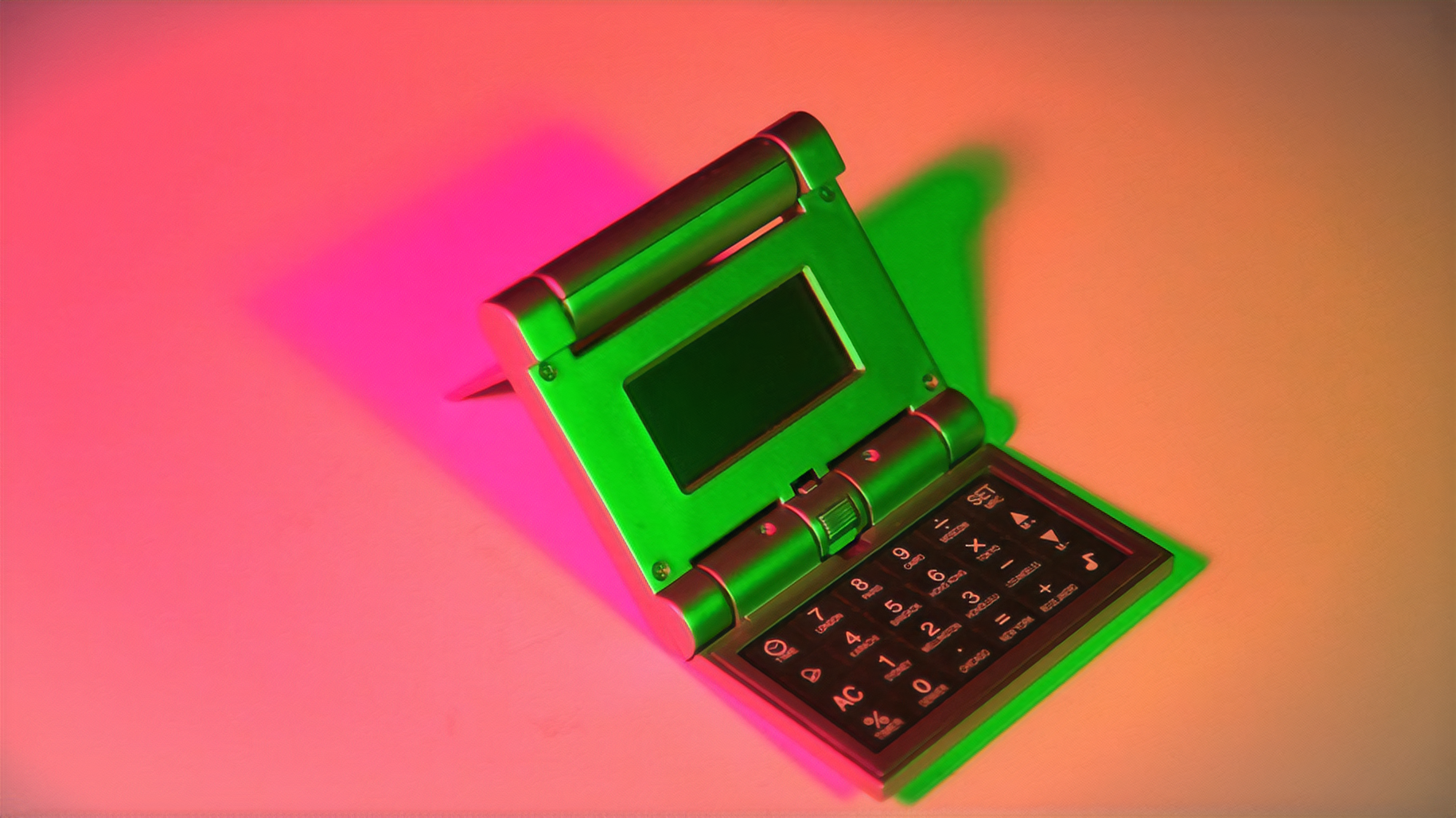 An open folding calculator, turned on its side and illuminated by bright green, peach, and pink lights.