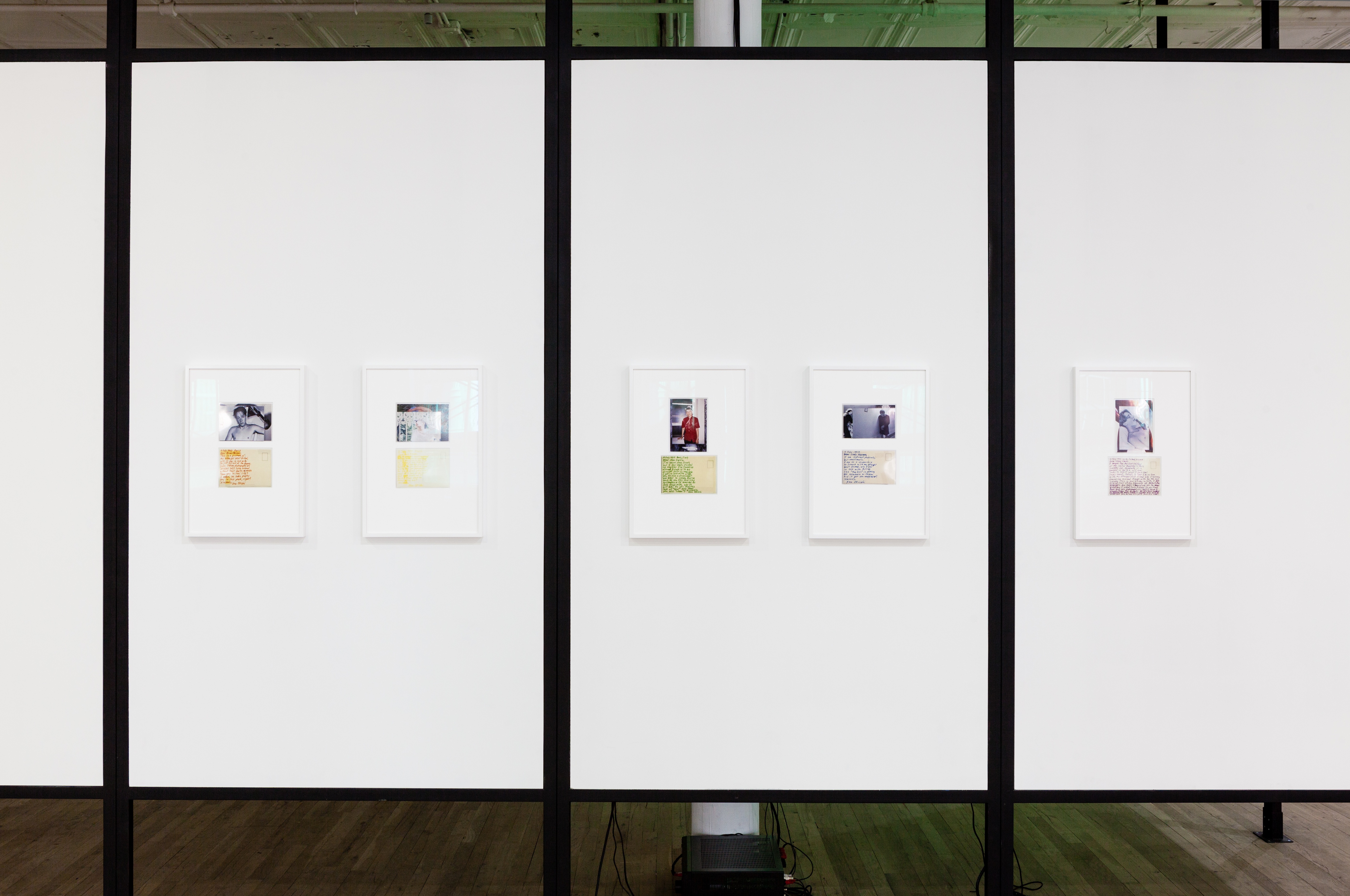 Five framed photographs and documents displayed on freestanding, white panels in an exhibition space.
