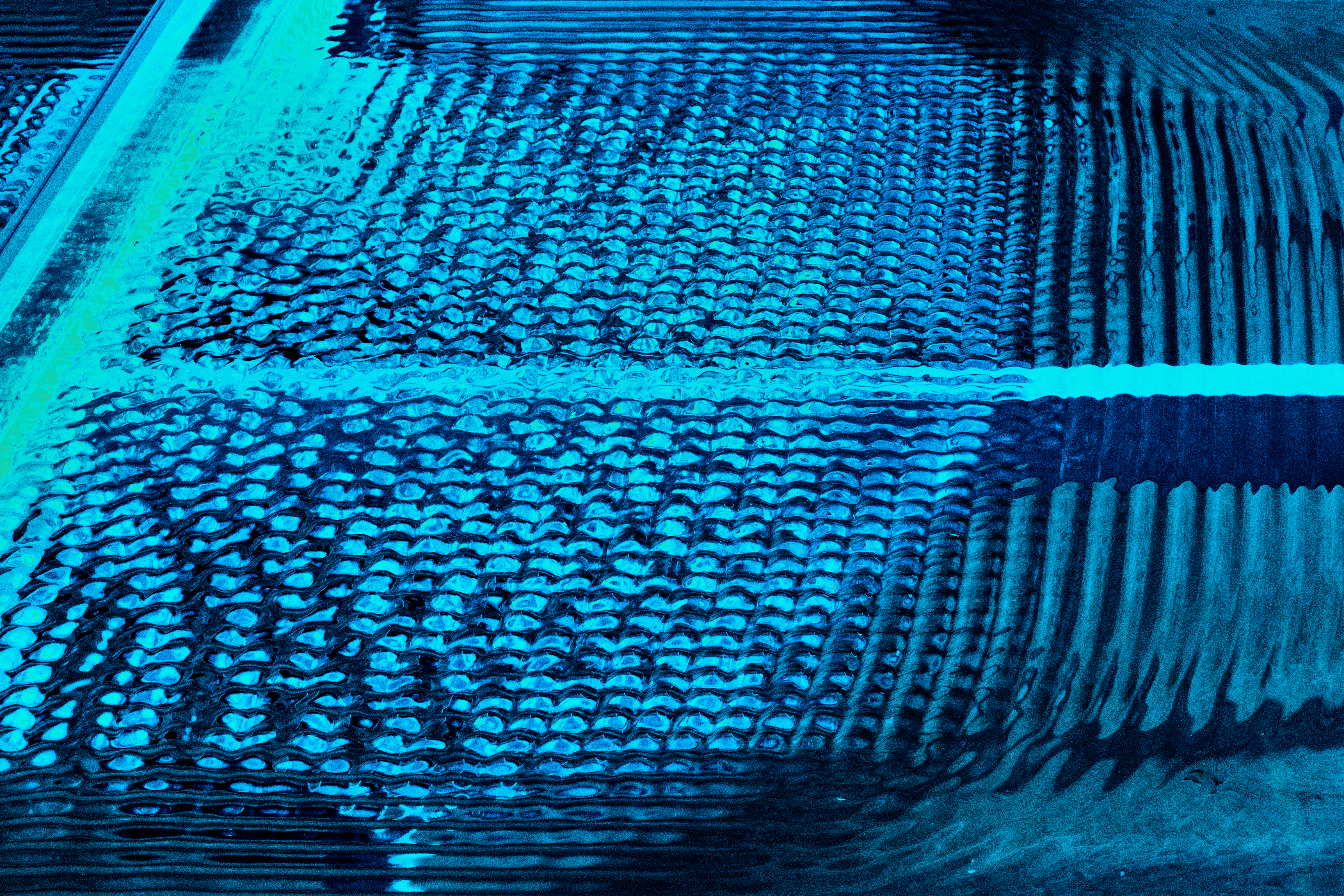 A close up photograph shows patterns of ripples in water, lit in iridescent blues.